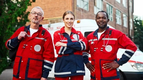 A female and two male paramedics in full gear posing in front of an ambulance ready to go into action.