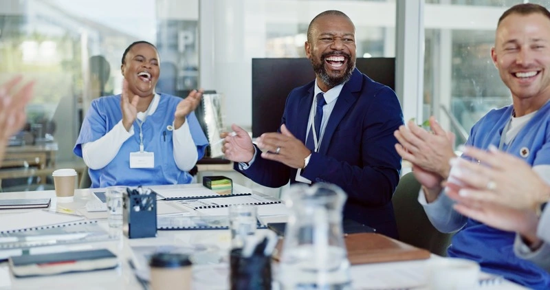 Happy team of healthcare professionals and an onsite staffing manager laughing together during a meeting at a medical facility.
